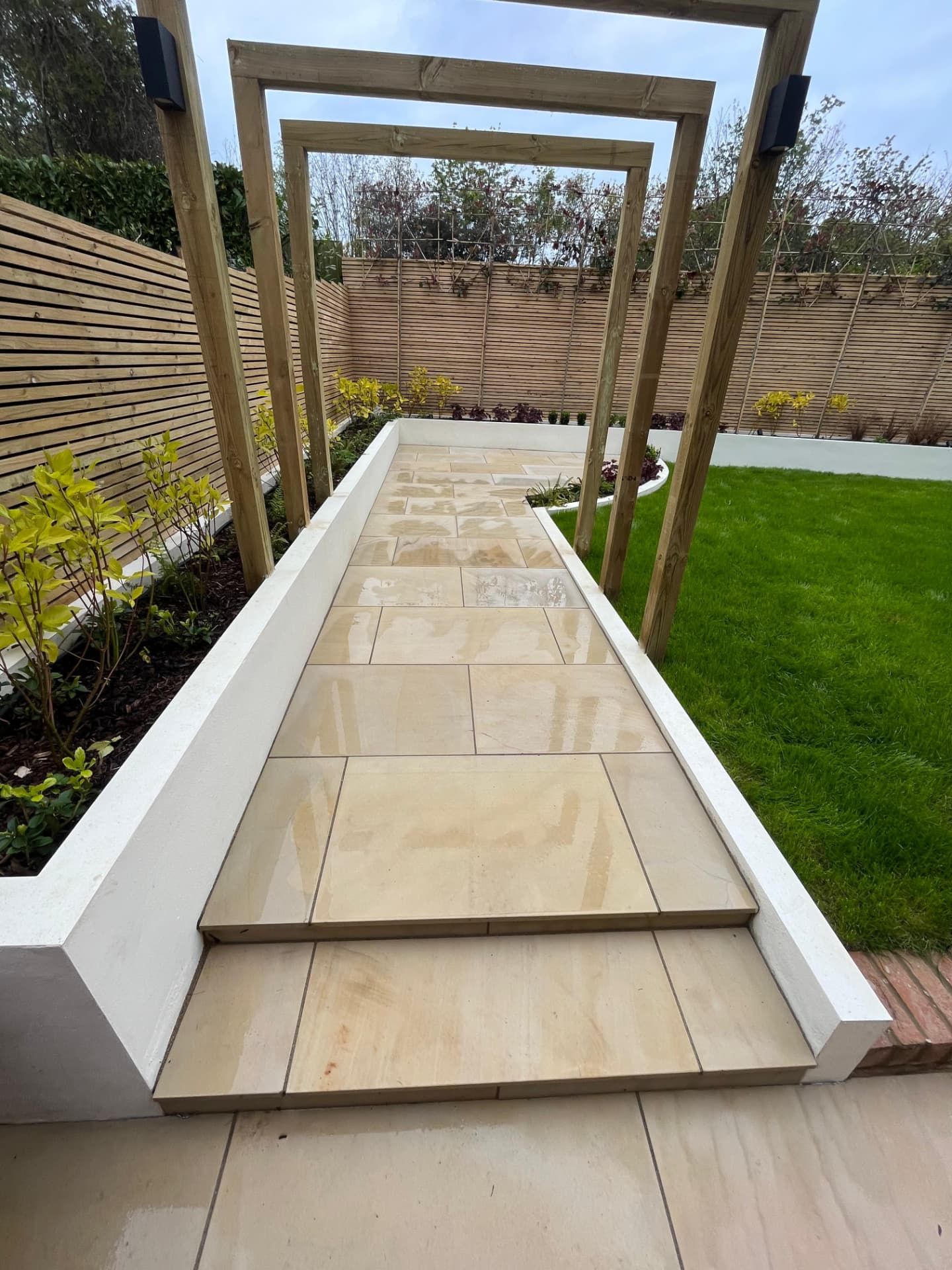 Sandstone steps and path under timber pergola arches beside a new lawn