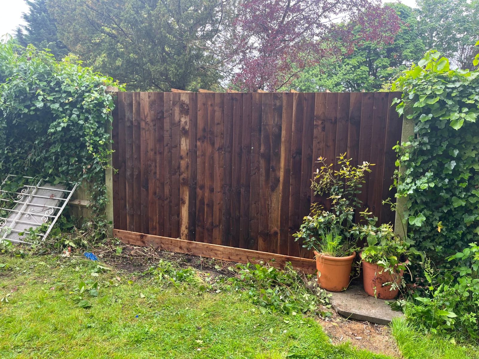 Dark stained closeboard fence with concrete posts and planted border
