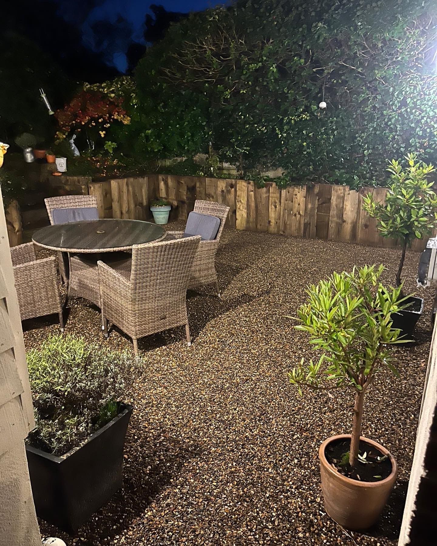 Gravel seating area lit at night with timber raised beds