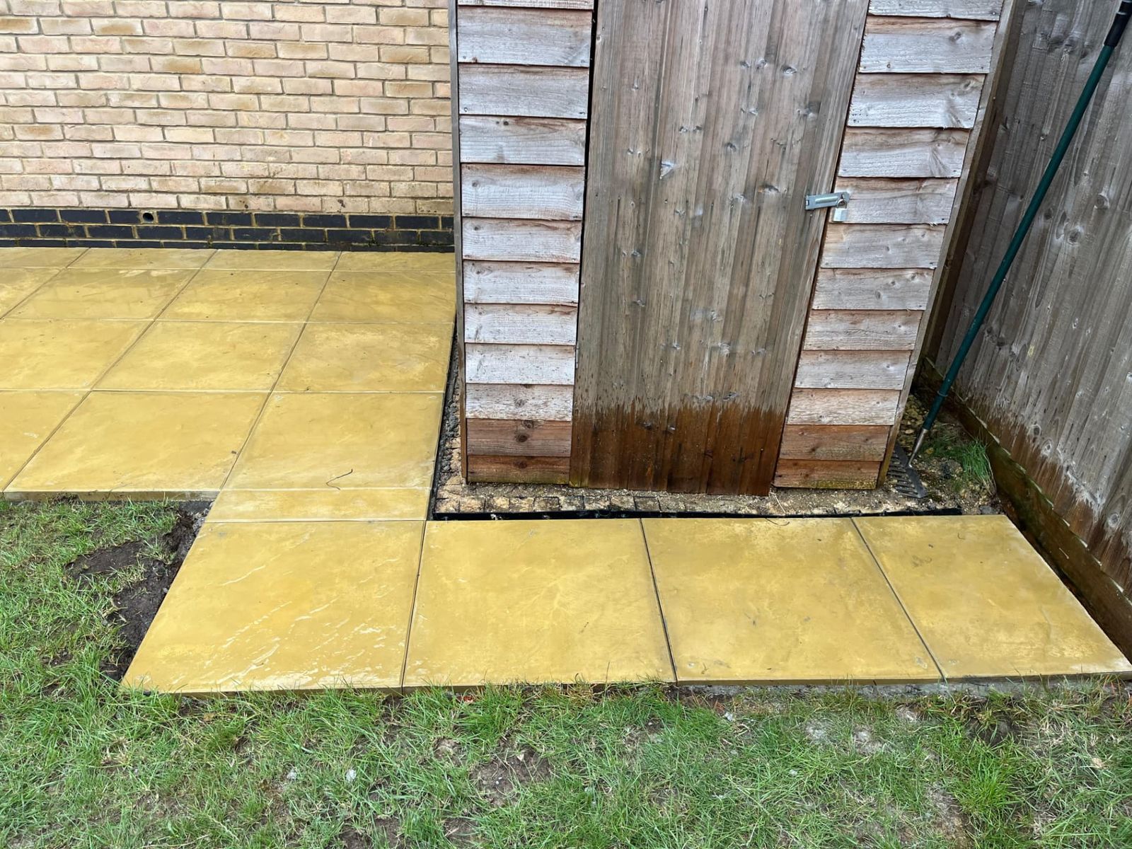Small warm sandstone patio beside a brick wall and timber shed